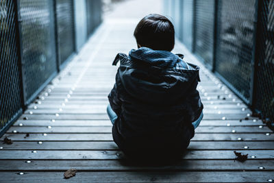 Rear view of boy sitting on bridge