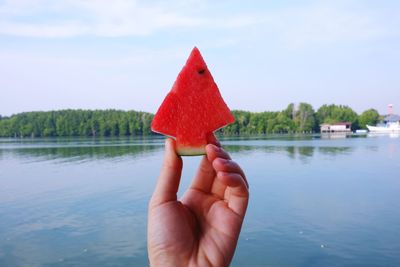 Close-up of hand holding watermelon against lake