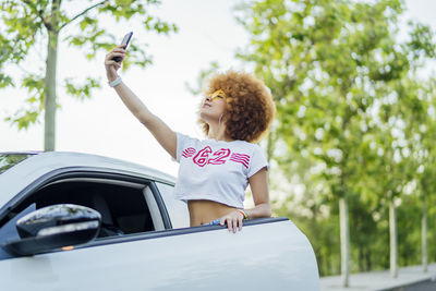 Woman with afro hair making a selfie next to her white car