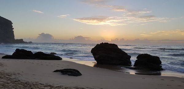 Rocks on beach against sky during sunset