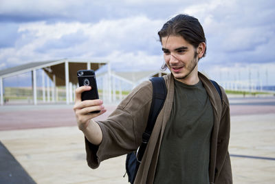 Man photographing while using smart phone against sky