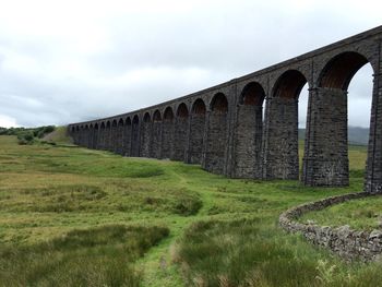 Ribblehead viaduct by grassy field against sky