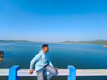 Young man sitting on the bridge and looking at blue river lake with blue sky scenery holiday concept
