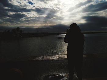 Silhouette woman standing at beach against sky during sunset