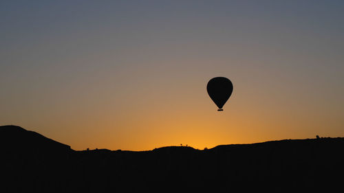 Silhouettes of a hot air balloon hovering over a mountain range. against the backdrop of  dawn sky.