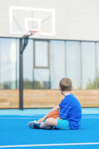 Boy sitting with basketball on sports court
