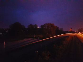 Illuminated street amidst buildings against sky at night