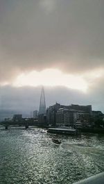 View of cityscape by sea against cloudy sky