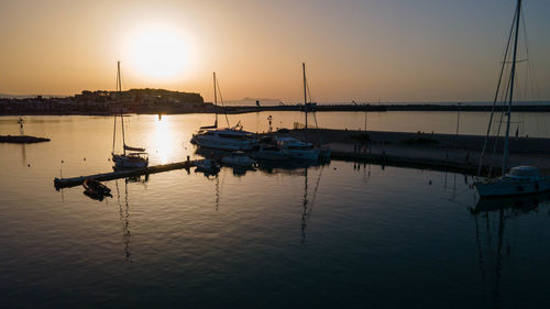 Sailboats moored in harbor at sunset