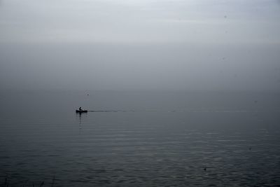 Man rowing boat in sea against sky during foggy weather