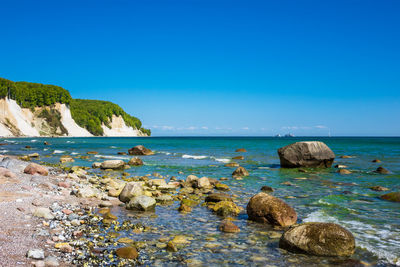 Rocks on beach against clear blue sky