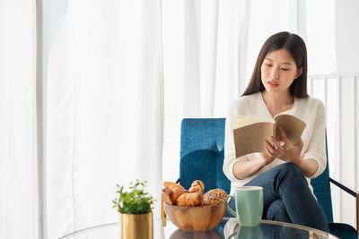 Young woman looking away while sitting on table at home