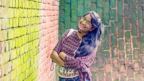 Portrait of smiling young woman standing against brick wall