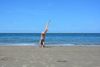 Full length of girl wearing swimwear doing handstand at beach