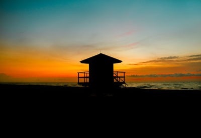 Silhouette hut by sea against sky during sunset