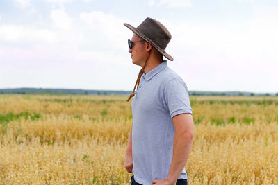 Crop and harvest. portrait of farmer standing in gold wheat field with blue sky in background. young