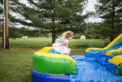 Girl in fairy costume jumping on bouncy castle at park during halloween