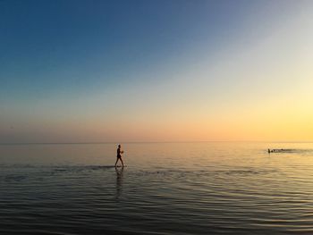 Mid distance of man walking in sea against sky during sunset