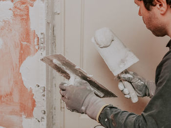 Hands in construction gloves caucasian guy applies fresh putty with two spatulas on the wall