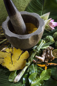 High angle view of herbs with mortar and pestle on leaf