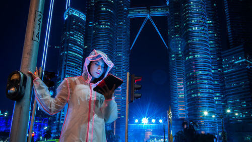 Woman using digital tablet against illuminated buildings in city at night