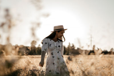 A girl in a wheat field wearing a dress and a straw hat. the girl is circling in the field.