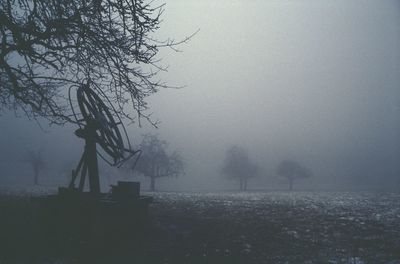 Bare trees on field against sky during foggy weather