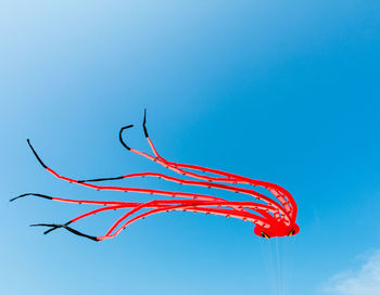 Low angle view of red octopus kite against blue sky