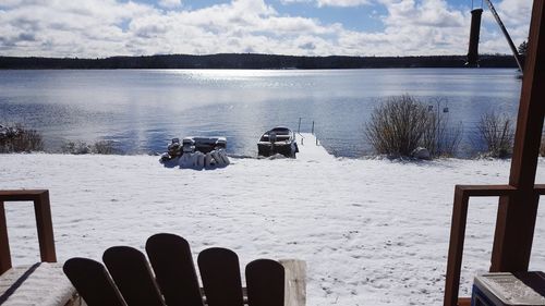 Low section of man sitting on snow covered lake against sky