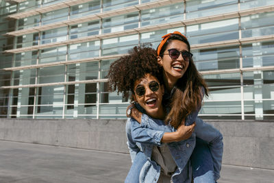 Mid adult woman piggybacking woman while standing on rooftop against building