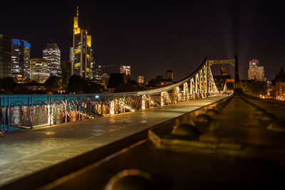 Illuminated bridge by buildings against sky at night