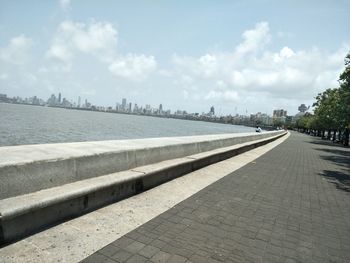 Footpath by river against sky in city