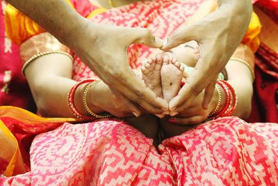 Cropped hands making heart shape against baby foot carried by woman