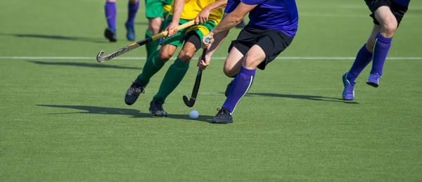 Low section of men playing hockey on turf