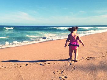 Girl walking at beach against sky