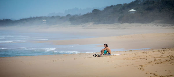 Man sitting at beach against mountains