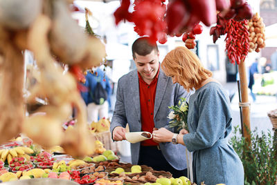 Young man and woman buying vegetables at market stall