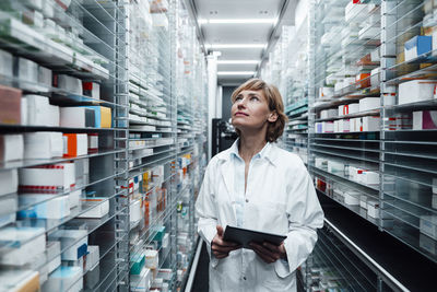 Female pharmacist looking at medicine while holding digital tablet at pharmacy store