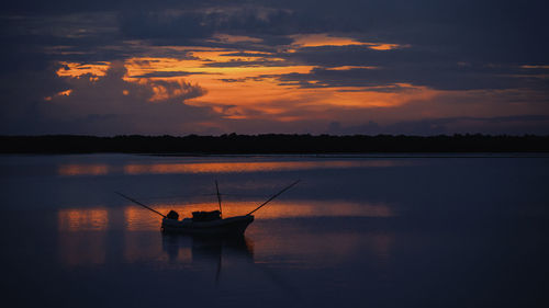 Silhouette man fishing in lake against sky during sunset