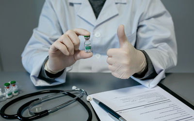 Midsection of doctor holding vaccine showing thumbs up