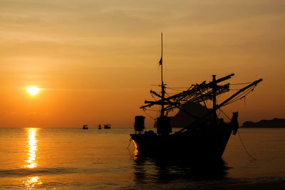 Silhouette sailboat in sea against orange sky