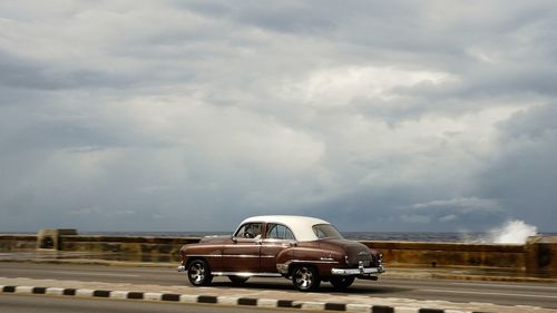 Vintage car on road against cloudy sky