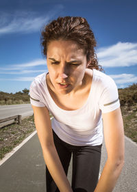 Young woman looking away while standing on road against sky