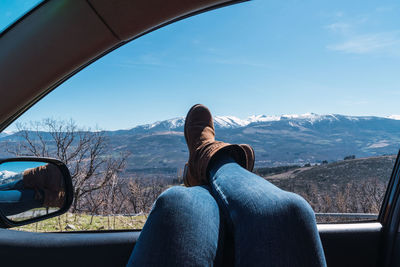 Female's feet sticking out of car window with a beautiful view of mountains under a clear sky