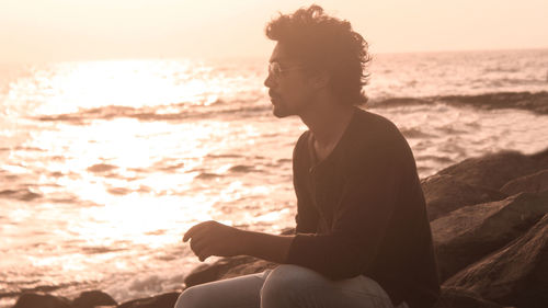 Man sitting on rock at beach during sunset