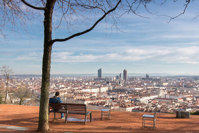 View of people sitting on bench in city against sky