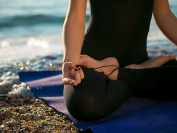 Low section of woman doing yoga at beach