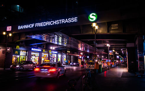 Illuminated cars moving on street by stores in city at night