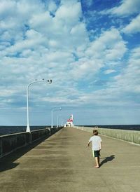 People walking on road by sea against sky