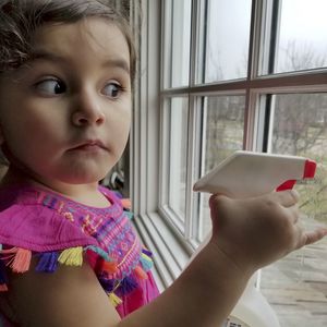 Cute girl holding spray bottle against window